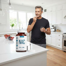 TRUEVANTAGE NUTRITION NAC 1000mg supplement bottle on a kitchen counter with a man taking a capsule in the background.